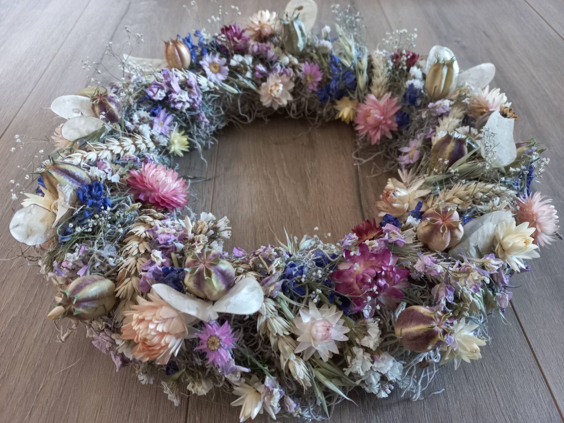 Krans gemaakt van gedroogde bloemen in verschillende kleuren, op een houten ondergrond.