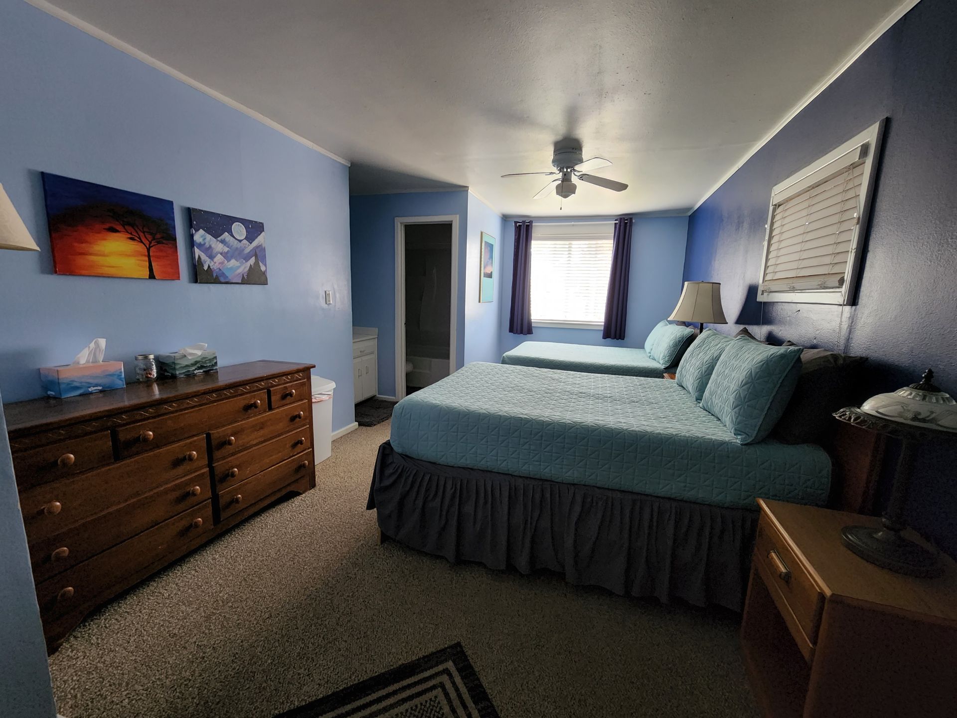 A bedroom with two beds , a dresser , and a ceiling fan.