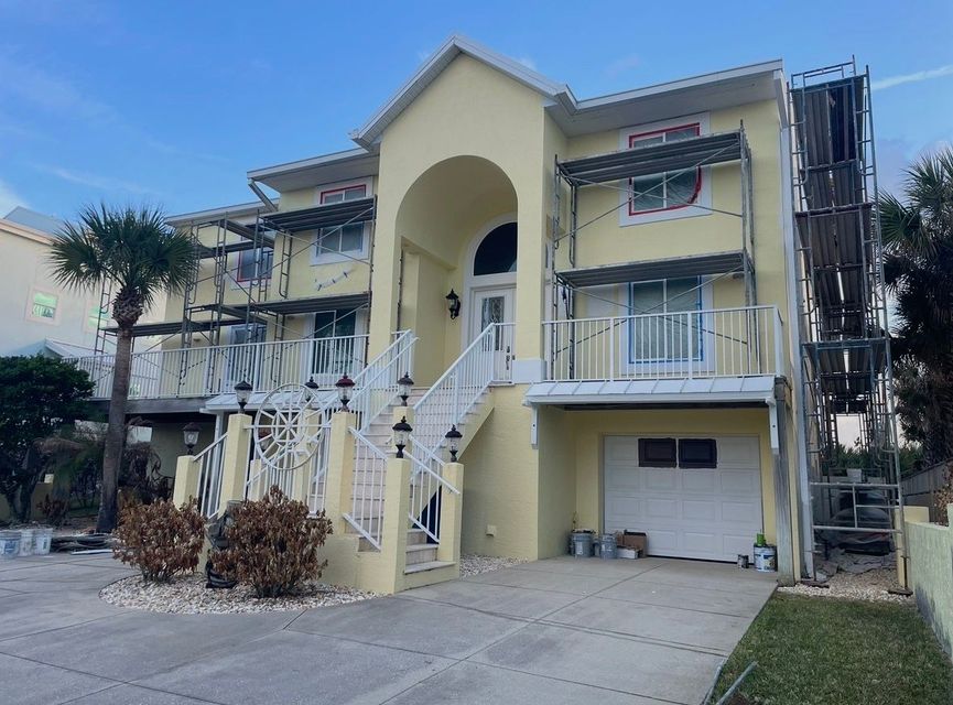 Two-story yellow house with damaged front stairs and balcony, garage below, in a residential neighborhood