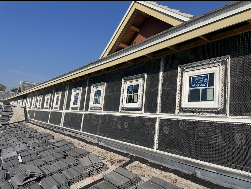 Long building under construction with black mesh siding, white-trimmed windows, and exposed roof framing