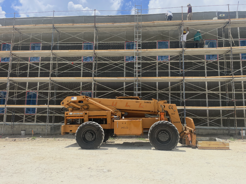 Orange construction lift in front of a scaffolded building under construction