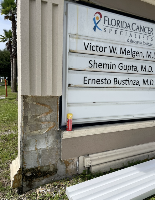 Florida Cancer Specialists sign on a building exterior with doctors’ names and a fire extinguisher nearby