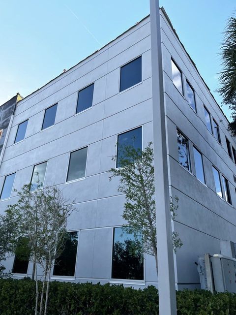 Modern white office building with blue windows and small trees outside