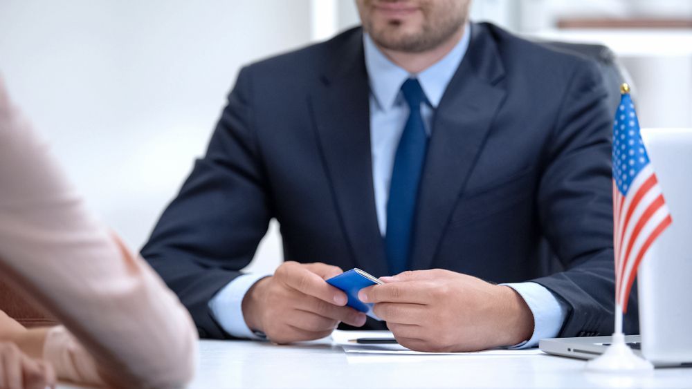Man in suit holding object at desk with American flag.