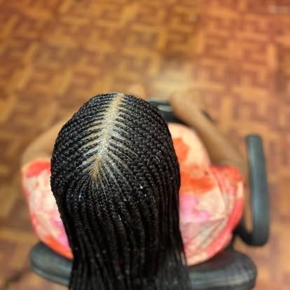 Top view of a person with long braided hair sitting in a chair, wearing a pink patterned top.