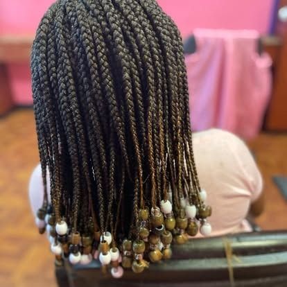 Close-up of long braided hair with white and gold beads, viewed from behind on a seated person