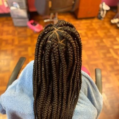 Person with long braided hair seated indoors on a chair, seen from behind.