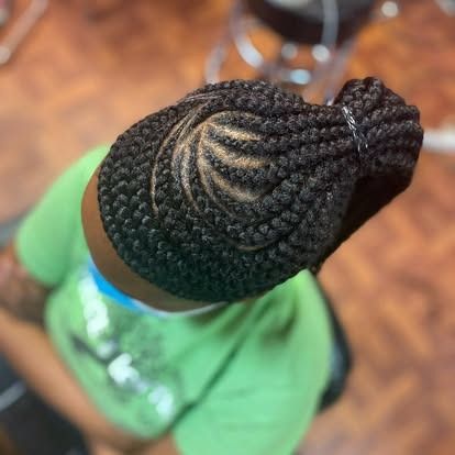 Top view of braided hair in a bun with a visible swirl parting, on a person wearing a green shirt.