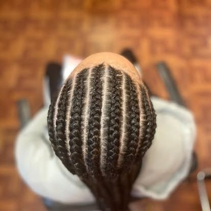 Top view of a braided hairstyle with neat cornrows and long braids, seated in a salon chair