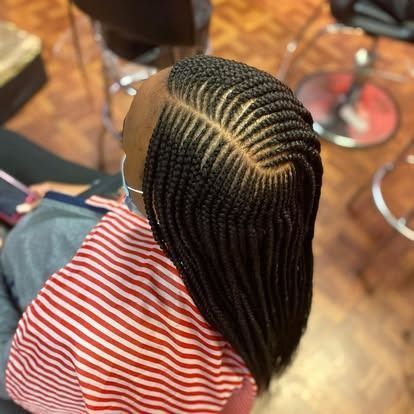 Close-up of braided hair with a geometric scalp pattern, next to a red-and-white striped shirt indoors.
