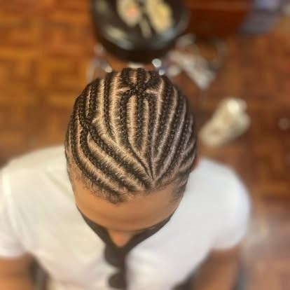 Top-down view of braided cornrows on a person wearing a white shirt, against a blurred wooden background.
