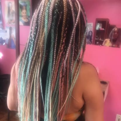 Person with long multicolored braids facing a pink bedroom mirror