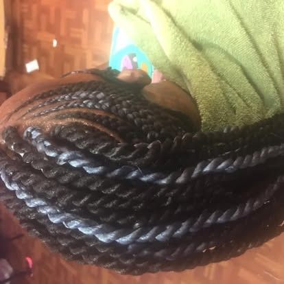 Close-up of long black braided hair resting on a green towel on a woven chair