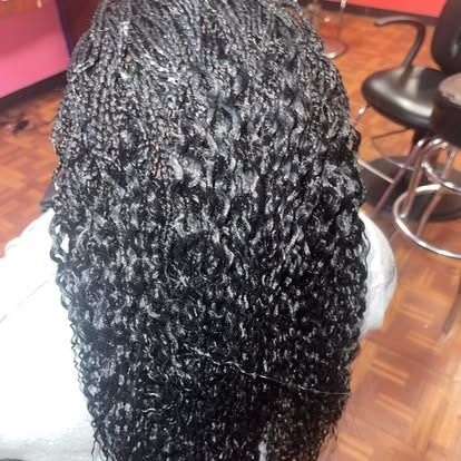 Close-up of long black braided hair from above in a salon chair, with pink walls and wooden floor in the background.