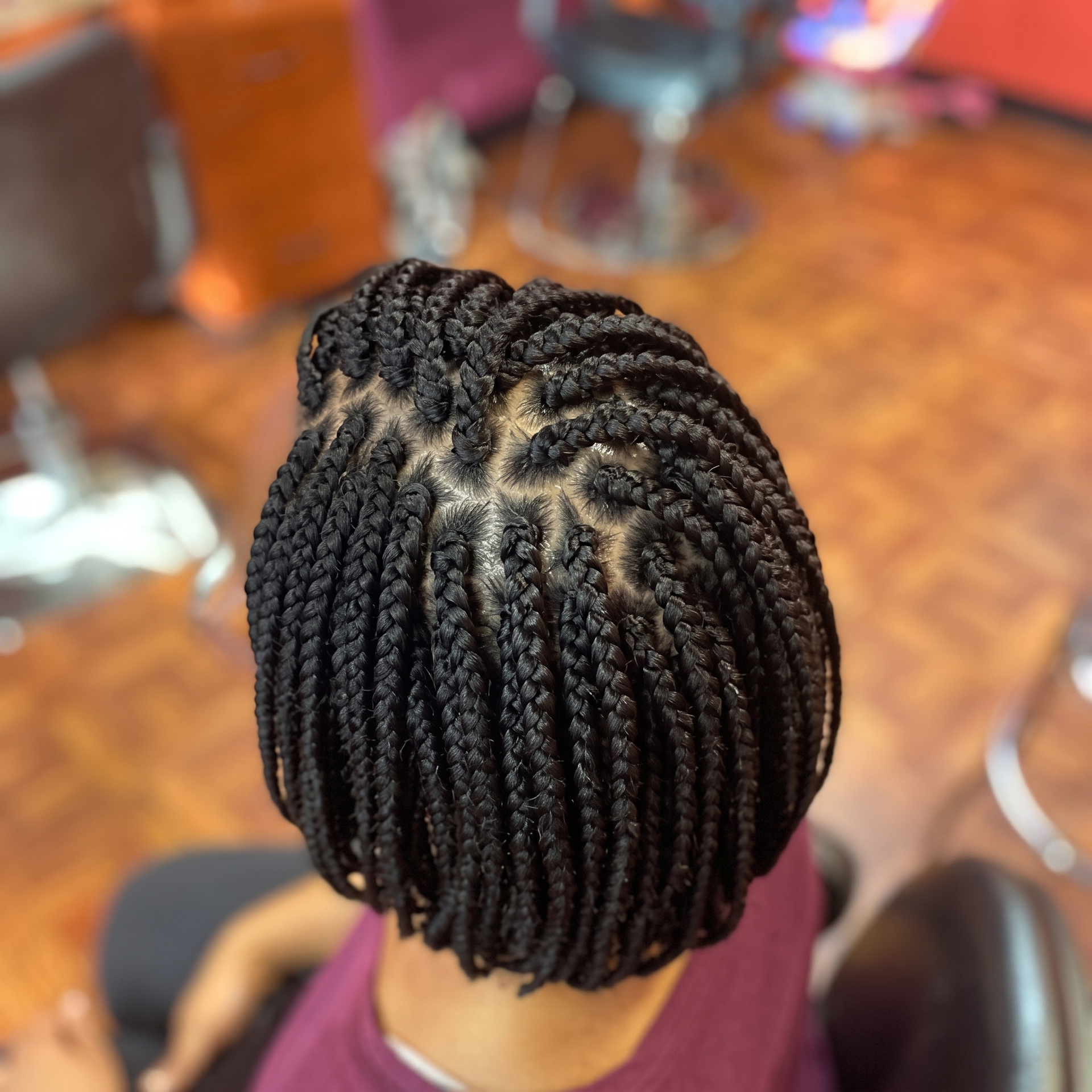 Close-up of neatly braided black hair at the crown, viewed from above in a salon setting