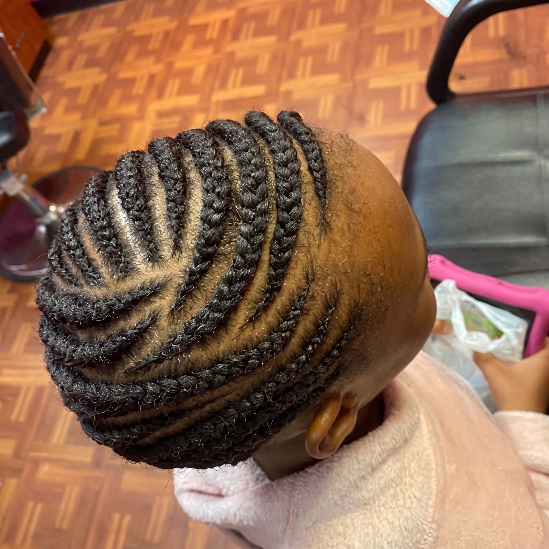 Child with neat braided cornrows, seated in a salon chair with a towel around the shoulders.
