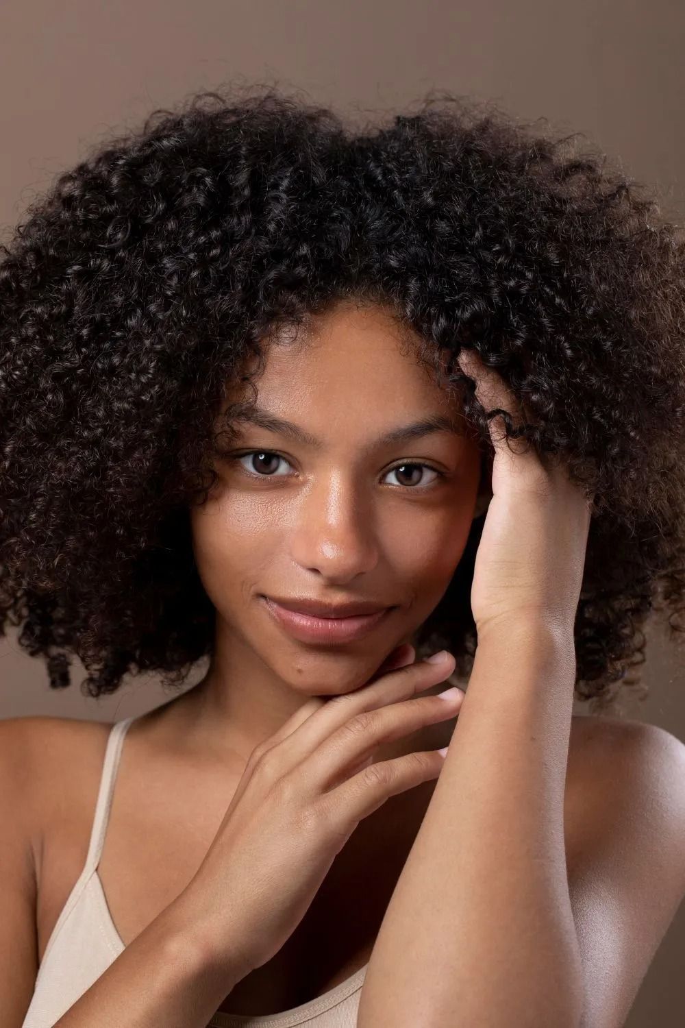 Portrait of a woman with curly hair resting her hand on her face against a soft brown background