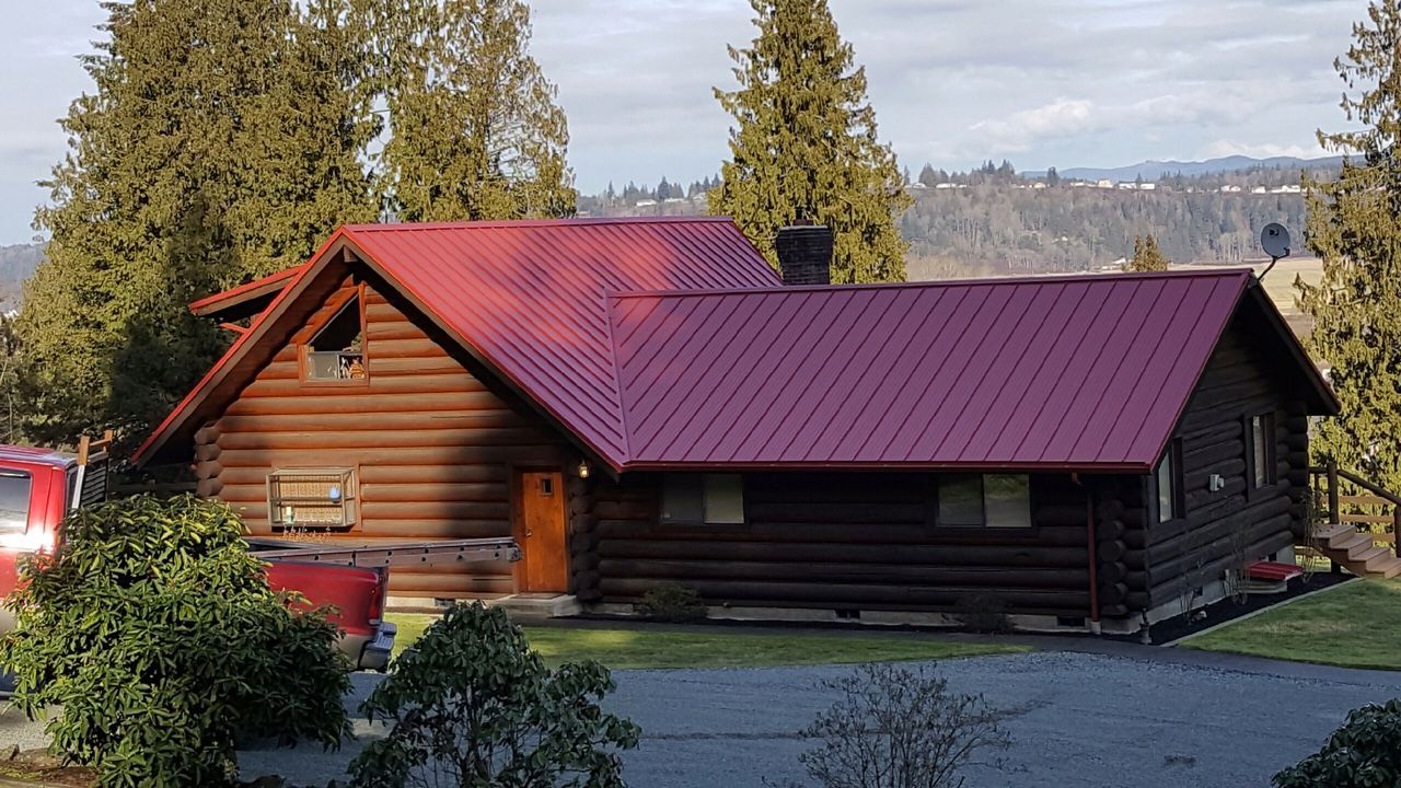 A log cabin with a red metal roof is surrounded by trees in Washington State