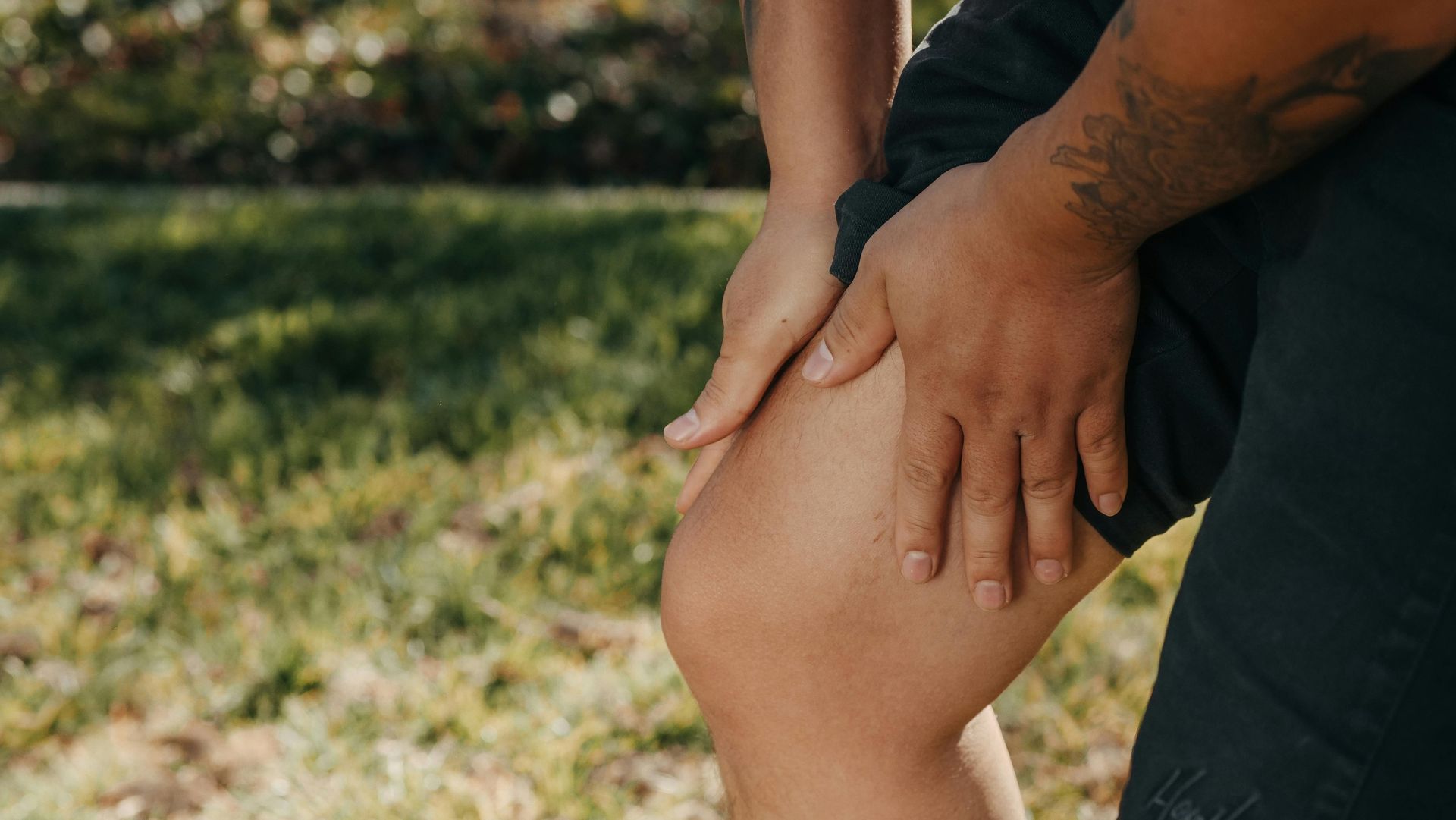 A person is holding their leg in pain while standing in the grass.