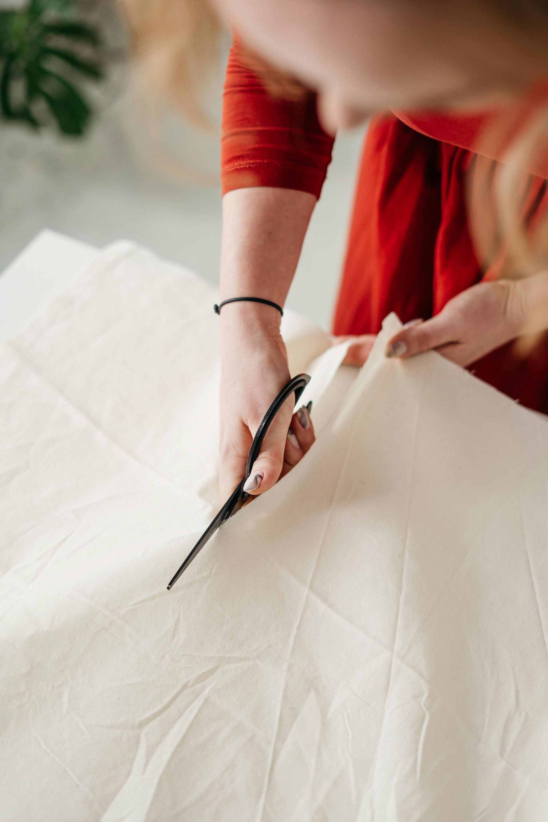 Woman in red shirt cutting fabric with scissors.