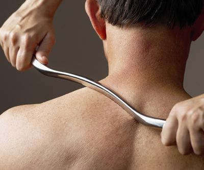 Person receiving back massage with a curved tool.
