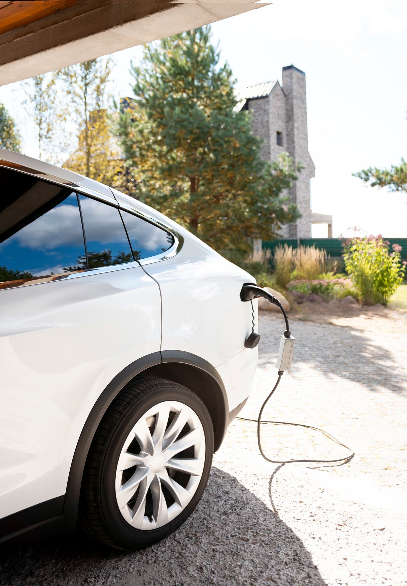 A white electric car is being charged in a driveway.