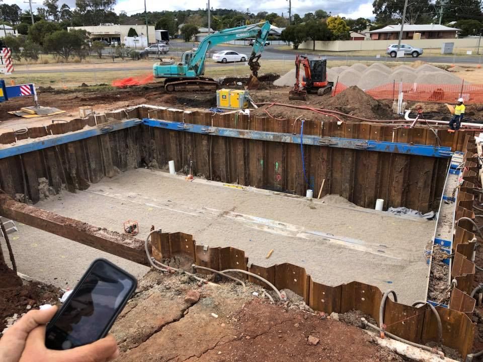 A Person Is Holding A Cell Phone In Front Of A Construction Site — JJ's Excavator & Tipper Hire in Kingaroy, QLD