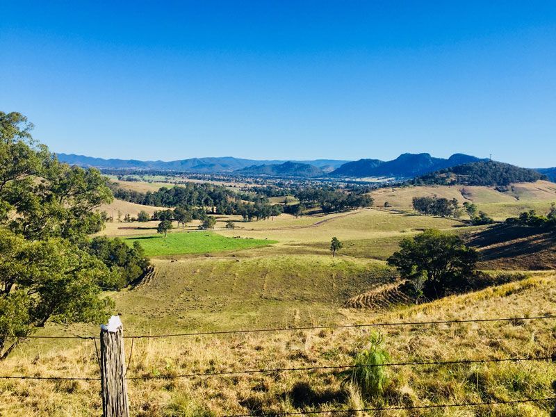 A Fence Surrounds A Lush Green Field With Mountains In The Background — JJ's Excavator & Tipper Hire in Murgon, QLD