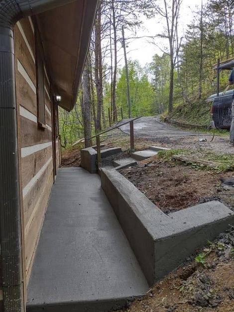 Concrete ramp beside a wooden cabin leading uphill through a wooded yard