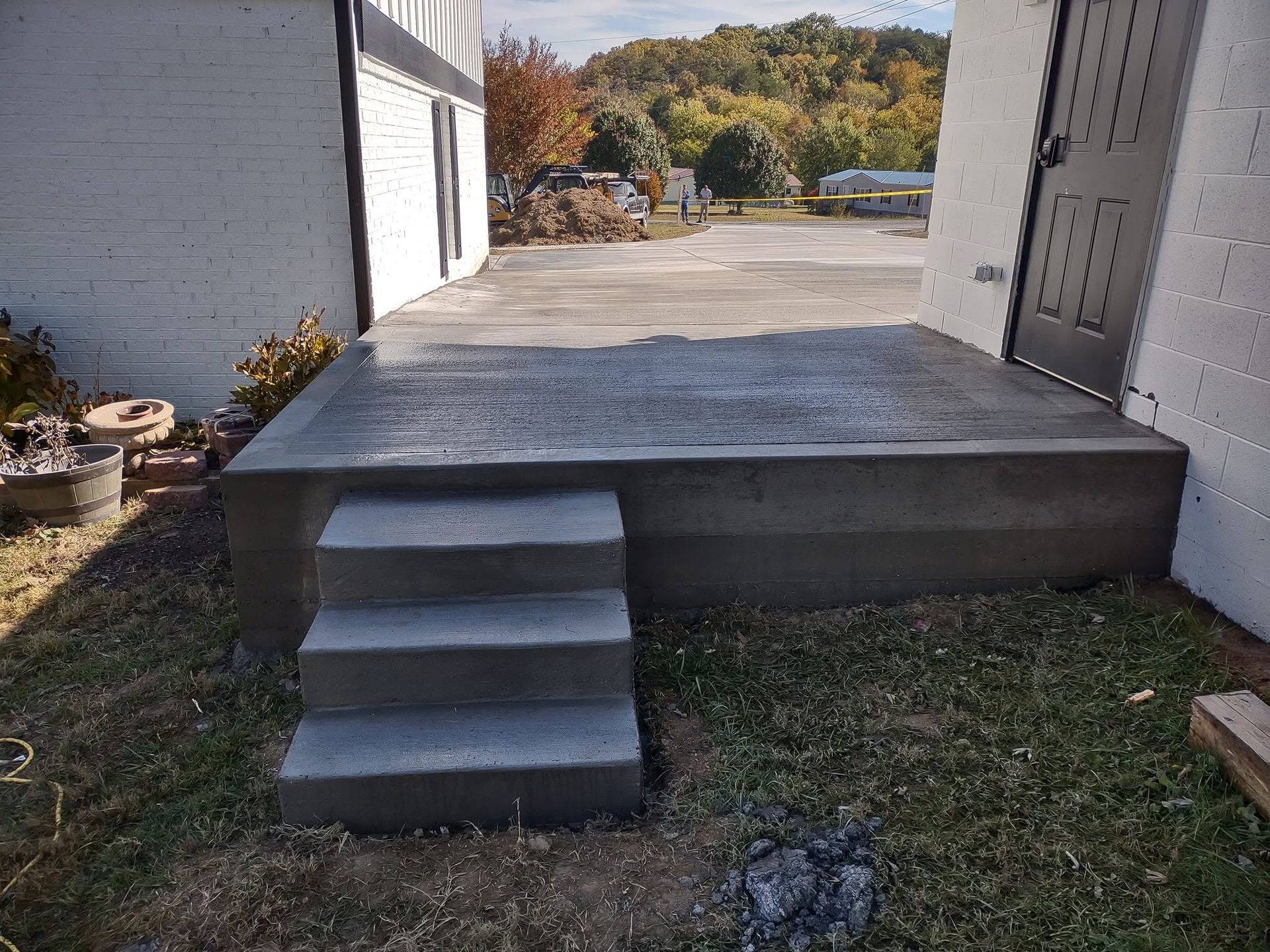 Concrete porch with three steps leading up to a raised deck beside a white building.