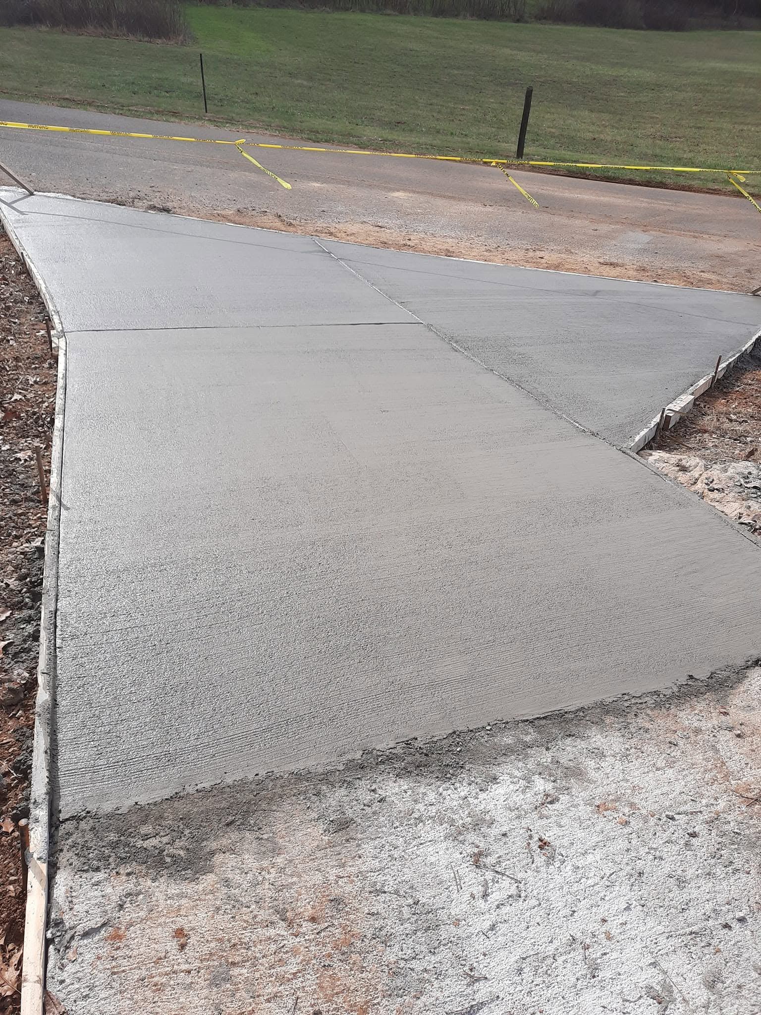 Cracked concrete sidewalk with a wet patch near a grassy roadside curb