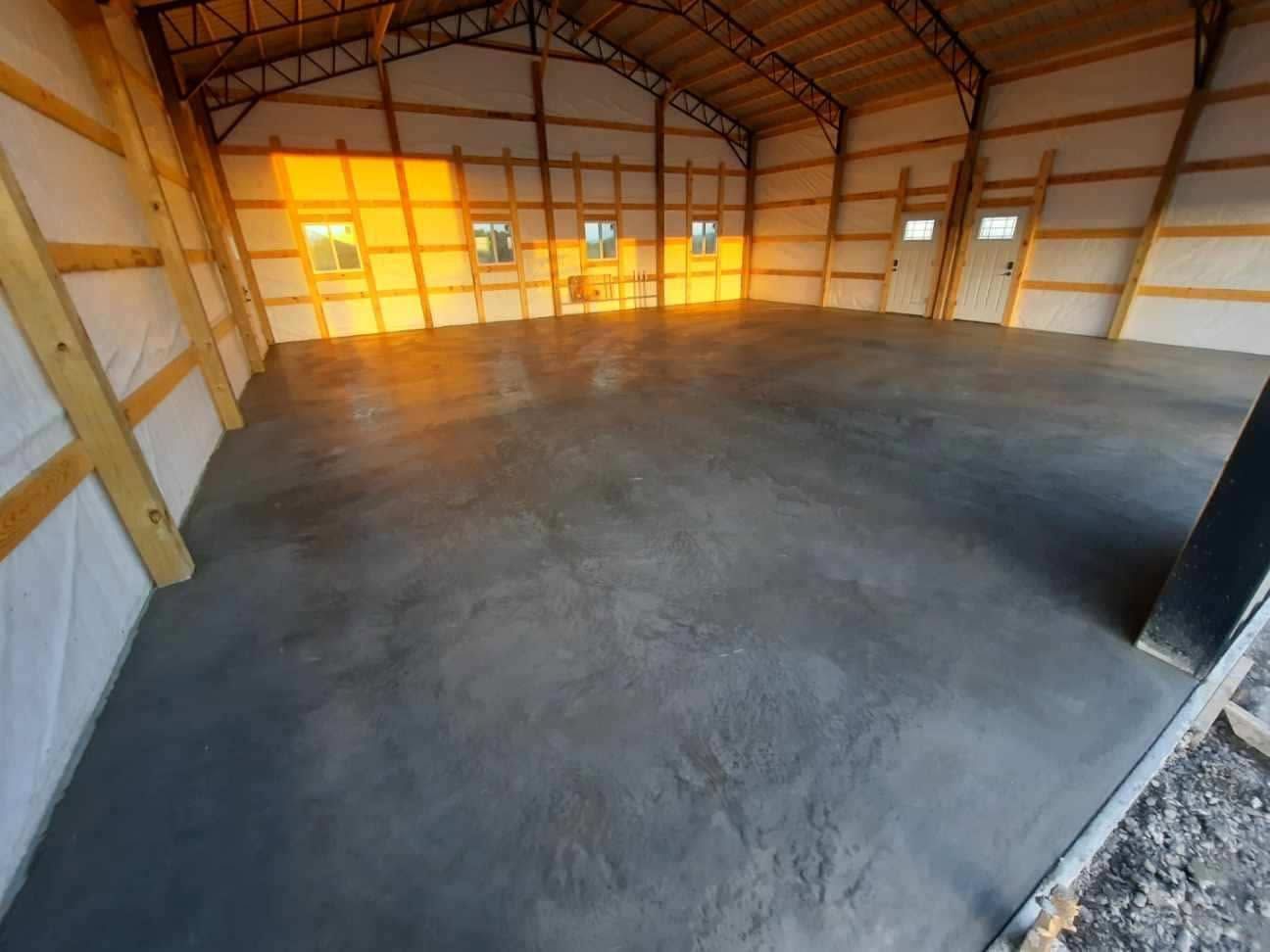 Empty unfinished garage with concrete floor and exposed wood framing, lit by warm sunlight.