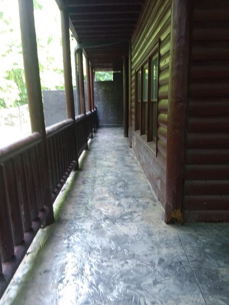 Wooden porch corridor with railings, log cabin walls, and a concrete floor, lit by daylight