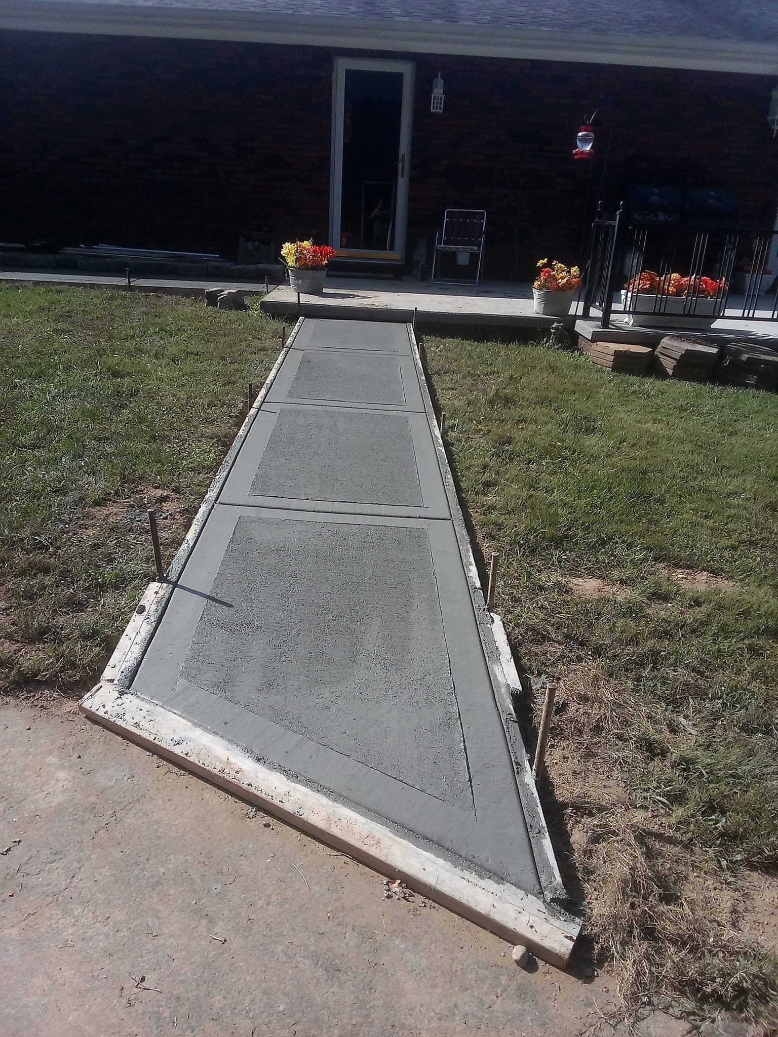 Concrete ramp leading to a house entrance, bordered by grass and flower pots.