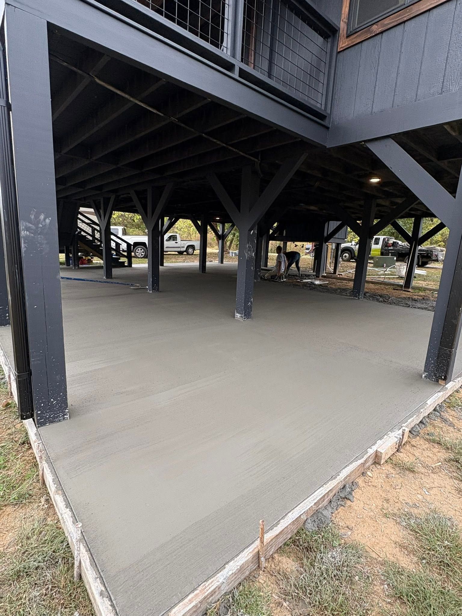 Empty concrete under a raised wooden structure with black support beams and nearby trees.