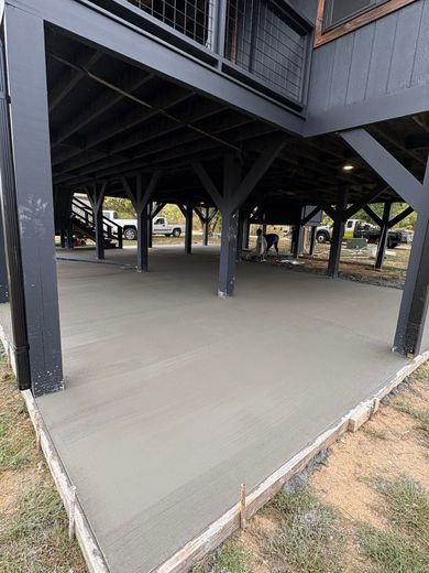 Empty concrete under a raised wooden structure with black support beams and nearby trees.