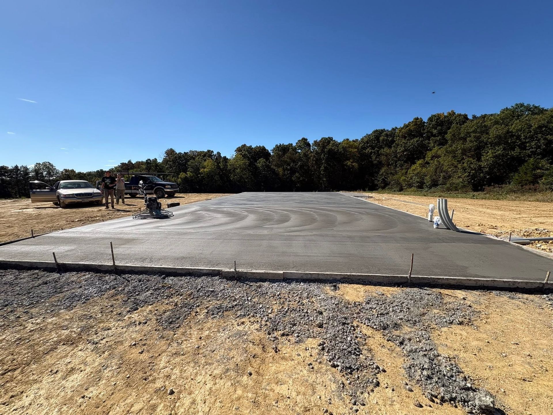 Freshly poured concrete driveway pad at a rural construction site under a clear blue sky