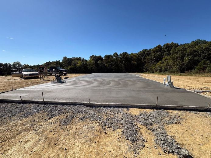 Freshly poured concrete driveway pad at a rural construction site under a clear blue sky