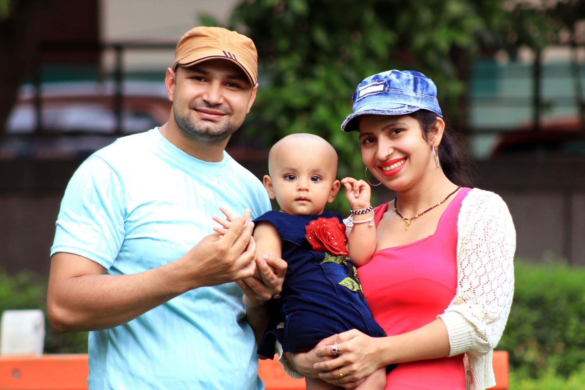 Mother and father are holding a baby between then. They are standing outside and both parents have hats on.
