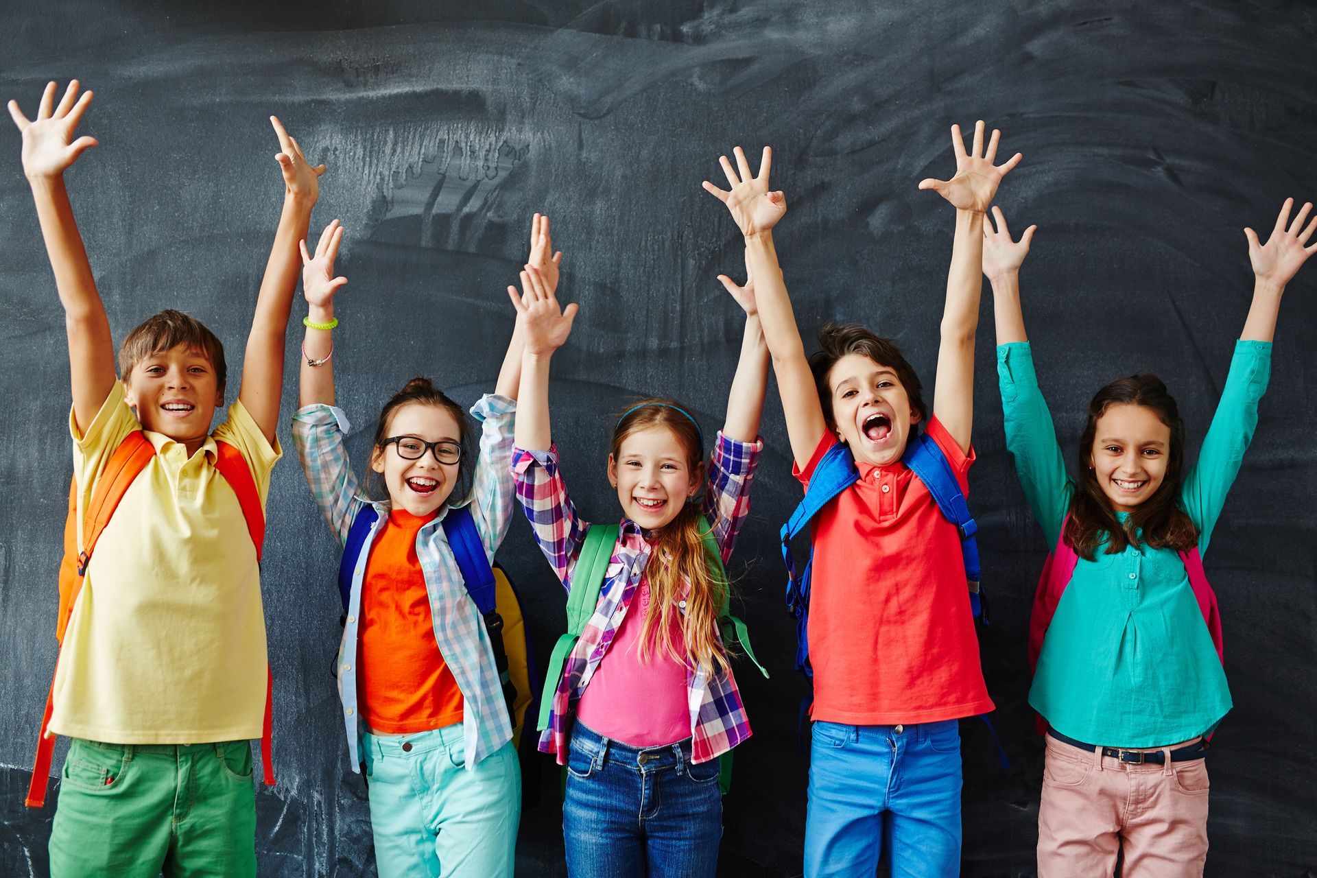 A group of children are standing in front of a blackboard with their hands in the air.