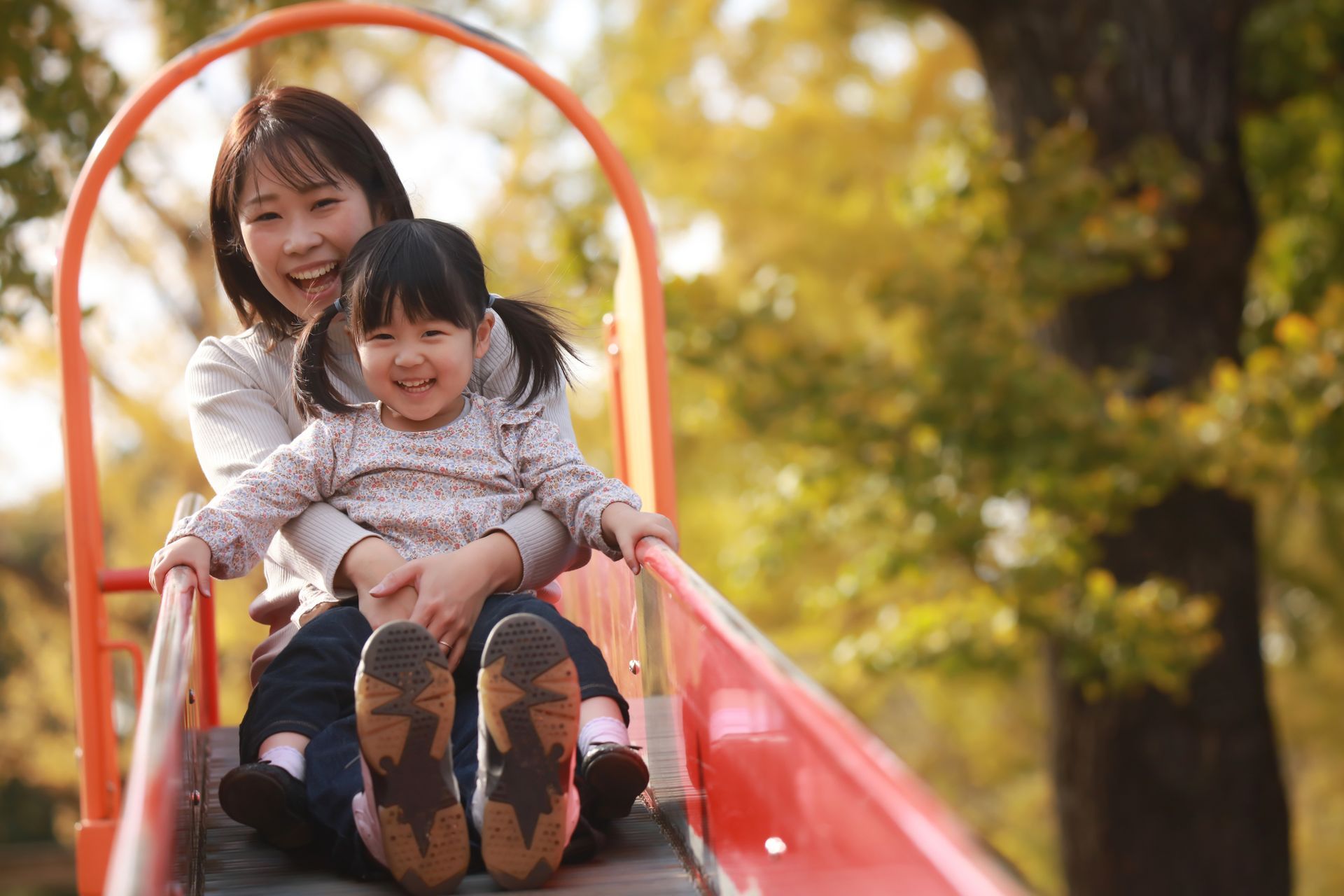 A woman and a little girl are riding a slide in a park.