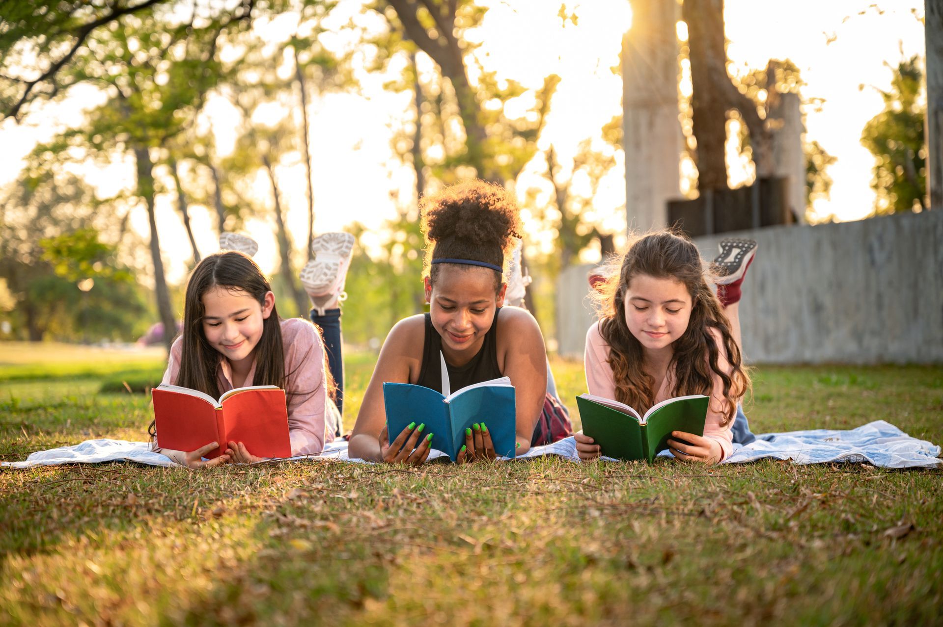 Three girls lying in the grass reading books