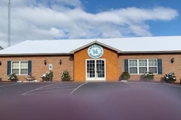 A brick building with a white roof and blue shutters is covered in snow.