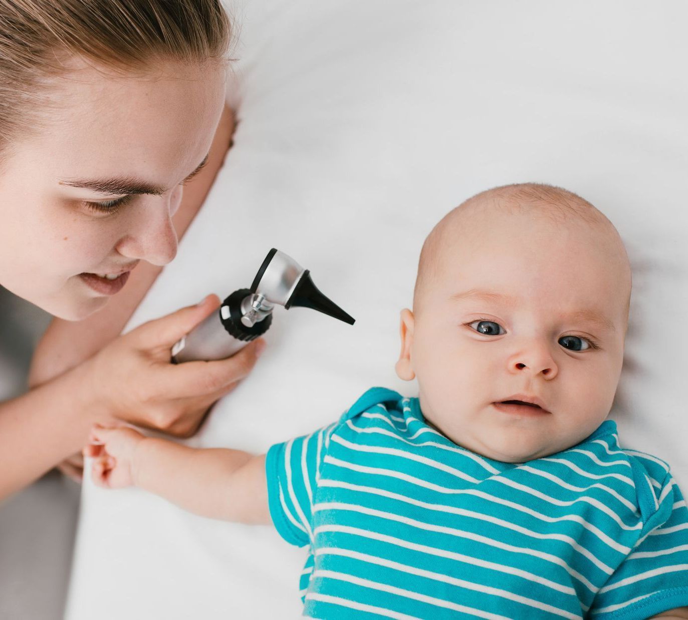 Medical professional giving pediatric care by checking the ears of a young baby.