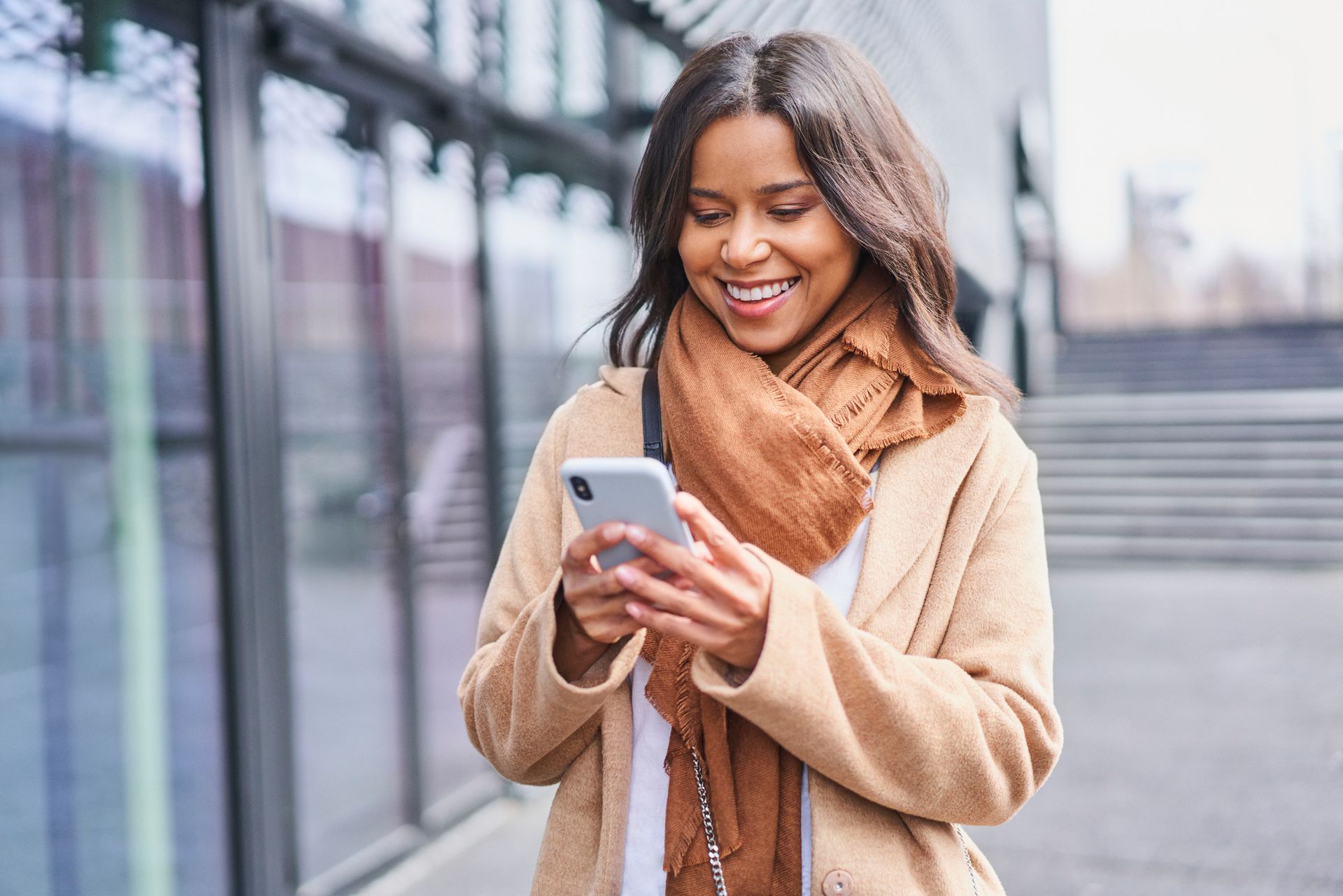 A woman in a coat and scarf is looking at her cell phone.