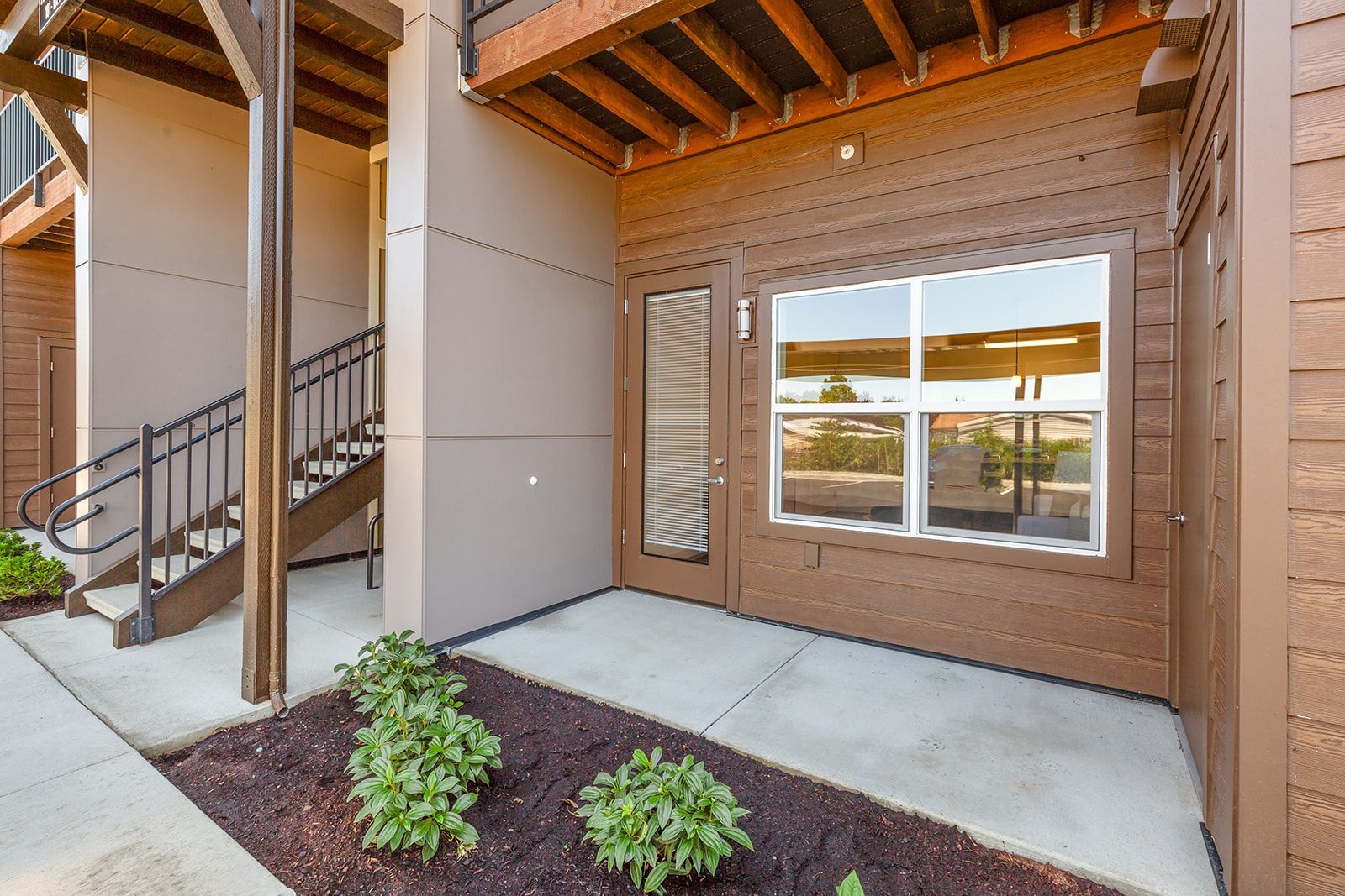 Covered apartment patio with concrete walkway, wooden beams, stairs, and a window overlooking a courtyard