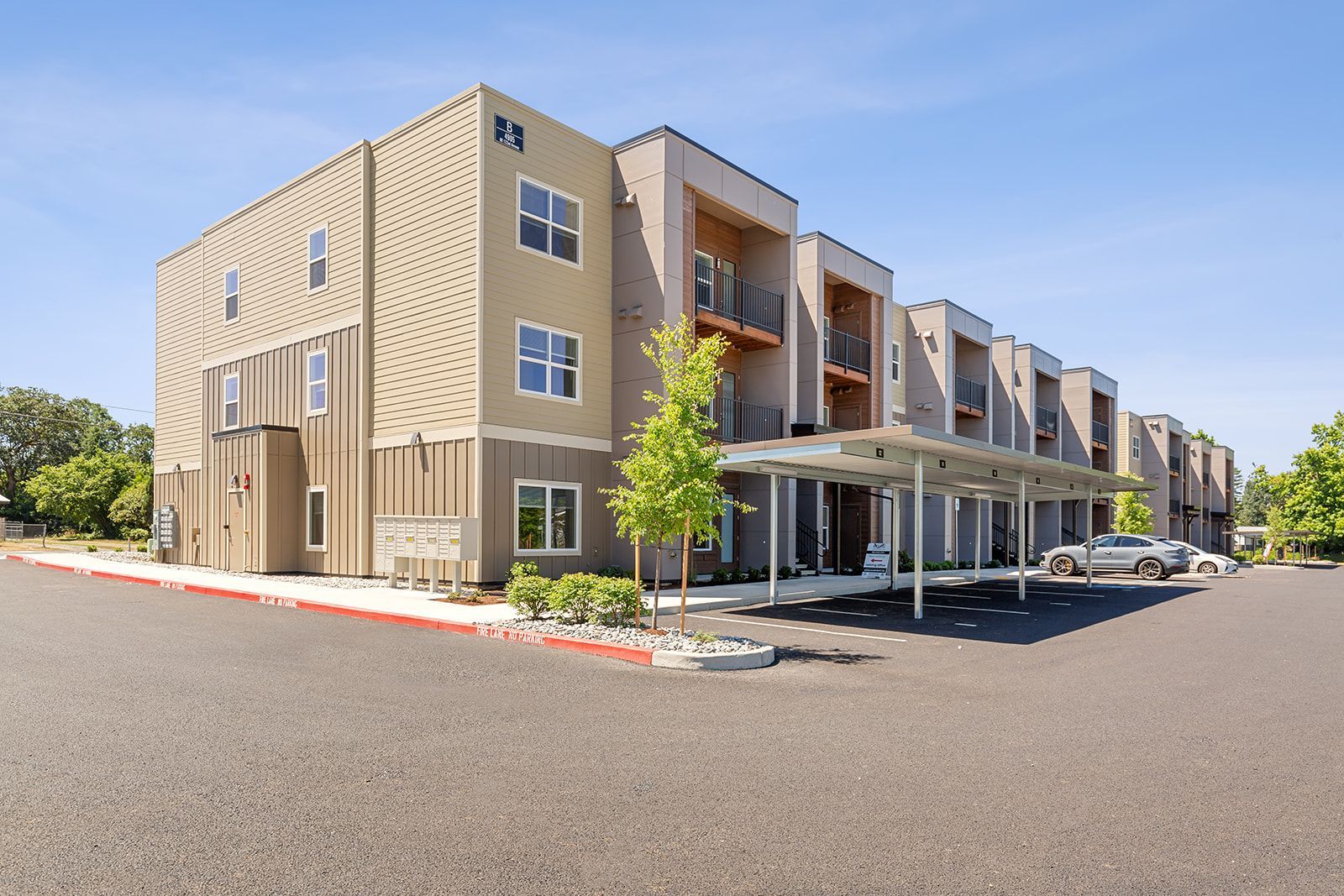 Modern apartment building exterior with covered parking and a large paved lot