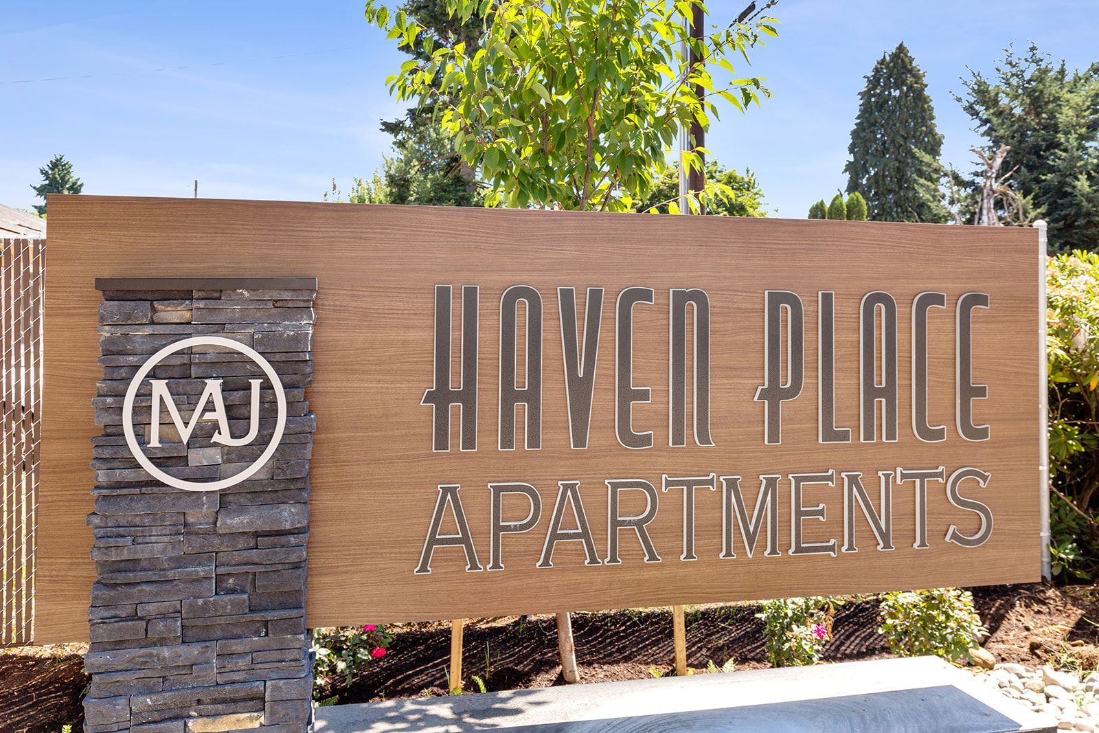 Sign for Haven Place Apartments with MJ logo on a wooden wall by landscaping