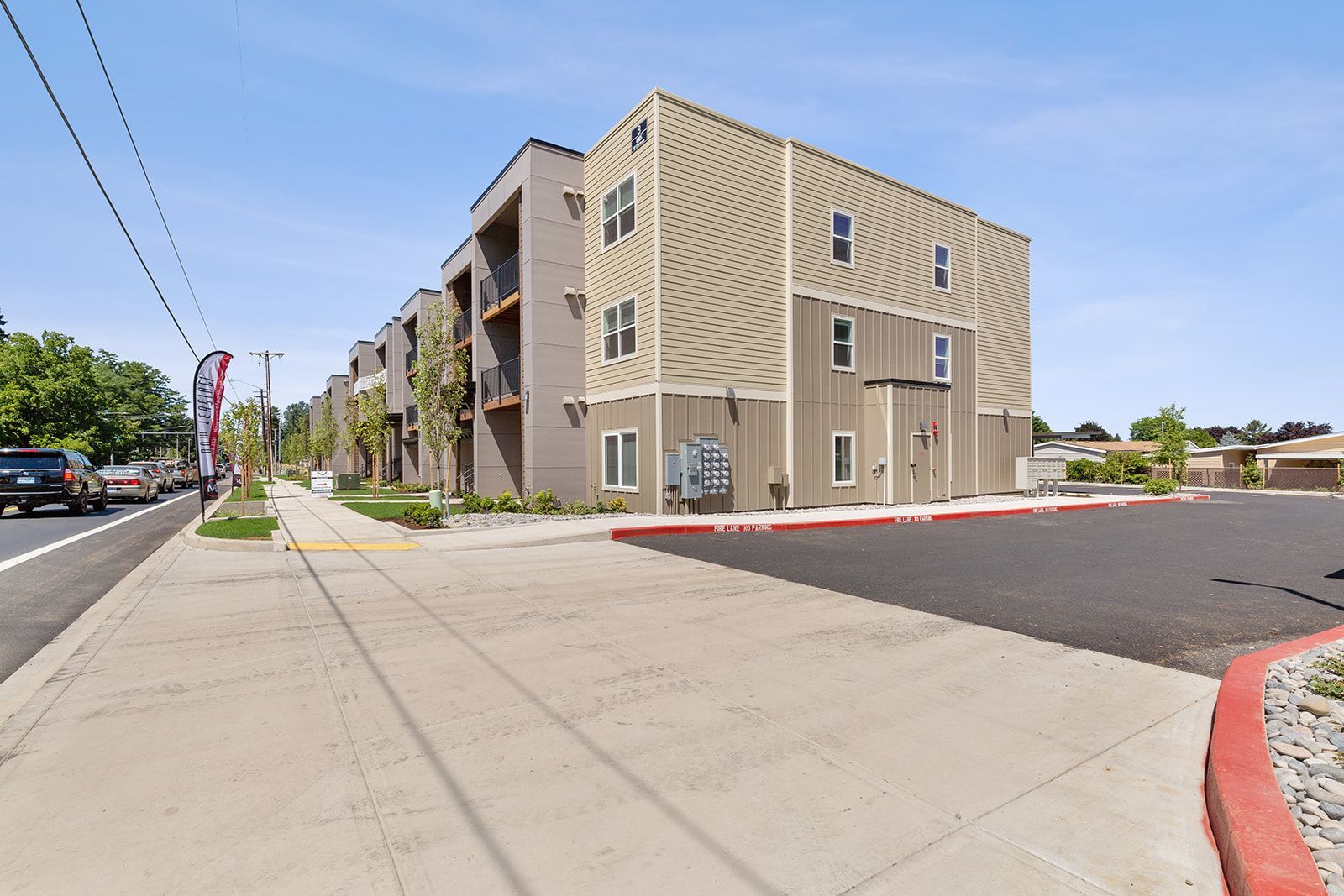 Modern apartment building beside a wide sidewalk and parking lot on a sunny street