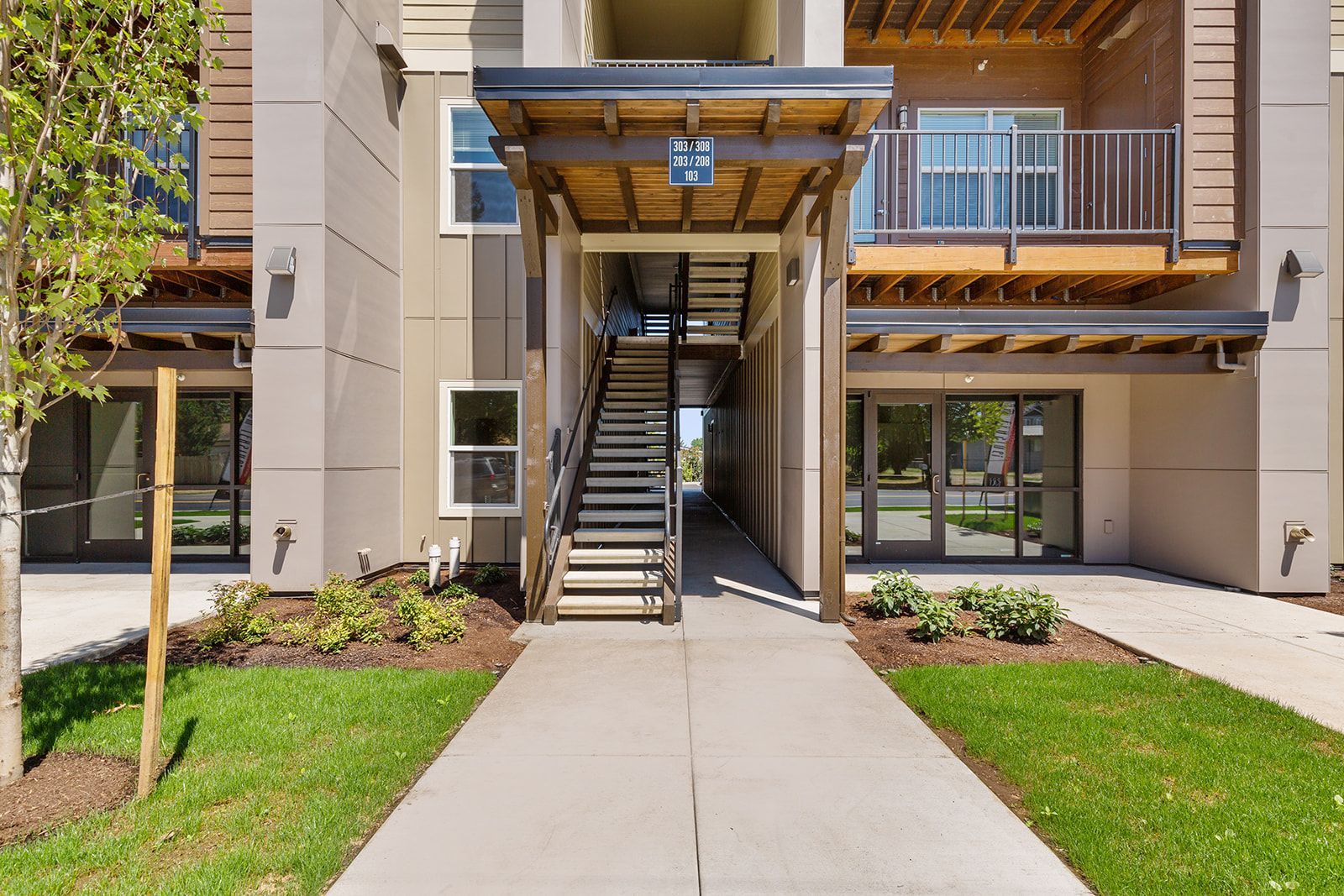 Apartment courtyard with central stairway, wooden balconies, and concrete walkways flanked by green lawns